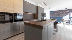 A modern kitchen with a central island, stainless steel appliances, and a dining area with bar stools. - StayCentral - Prahran Penthouse - Mount St, Prahran - 2 Bedrooms, 2 Beds, 2 Bathrooms, 1 secure parking spot and a permit for street parking. (Prahran)