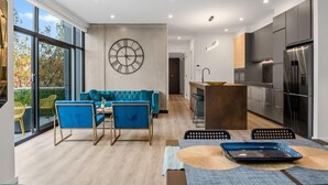 A modern kitchen with a large clock on the wall, a dining area with blue chairs, and a view through large windows. - StayCentral - Prahran Penthouse - Mount St, Prahran - 2 Bedrooms, 2 Beds, 2 Bathrooms, 1 secure parking spot and a permit for street parking. (Prahran)