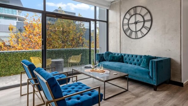 A modern living room with a large window, a blue sofa, and a coffee table. - StayCentral - Prahran Penthouse - Mount St, Prahran - 2 Bedrooms, 2 Beds, 2 Bathrooms, 1 secure parking spot and a permit for street parking. (Prahran)