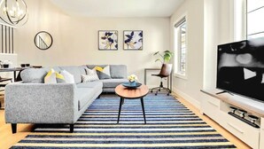 Un salon moderne avec un canapé gris, une table basse, un tapis à rayures et un téléviseur à écran plat.