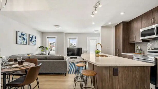 Une cuisine moderne dotée d’un îlot central, de tabourets de bar et d’un coin repas comprenant un canapé et une table.