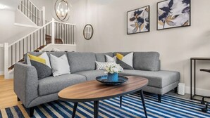Un salon moderne avec un canapé d’angle gris, une table basse en bois et un tapis à rayures bleues.