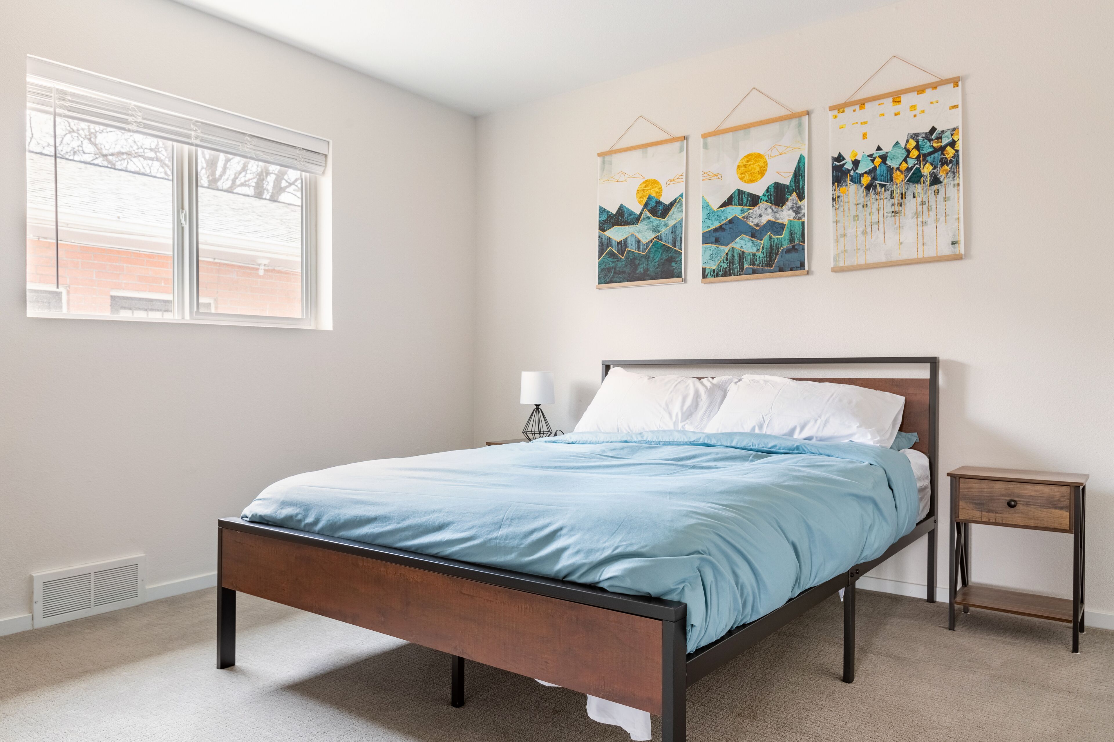 A bedroom with a bed, bedside table, and wall art.