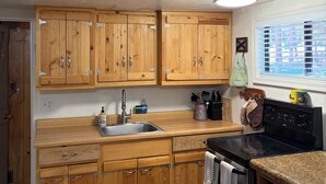 A kitchen with wooden cabinets, a stainless steel sink, a stove, and a window with blinds. - Bell's Greer Hideaway (Greer)