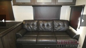 A black leather sofa with a cushioned backrest and armrests, positioned against a wall with a wooden cabinet above. - Lake St Clair Waterfront (Chesterfield)