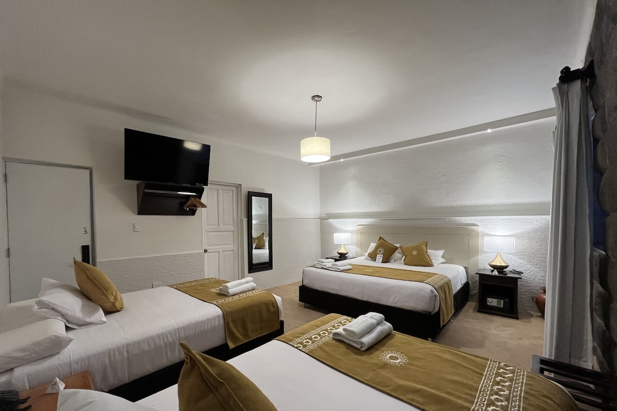 A hotel room with two beds, a TV mounted on the wall, and a bedside table with a lamp.