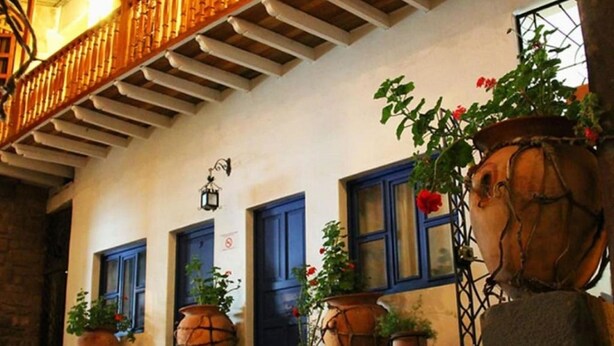 Un bâtiment au décor intérieur rustique, avec un escalier en bois, de grands pots en terre cuite ornés de plantes et des portes bleues.