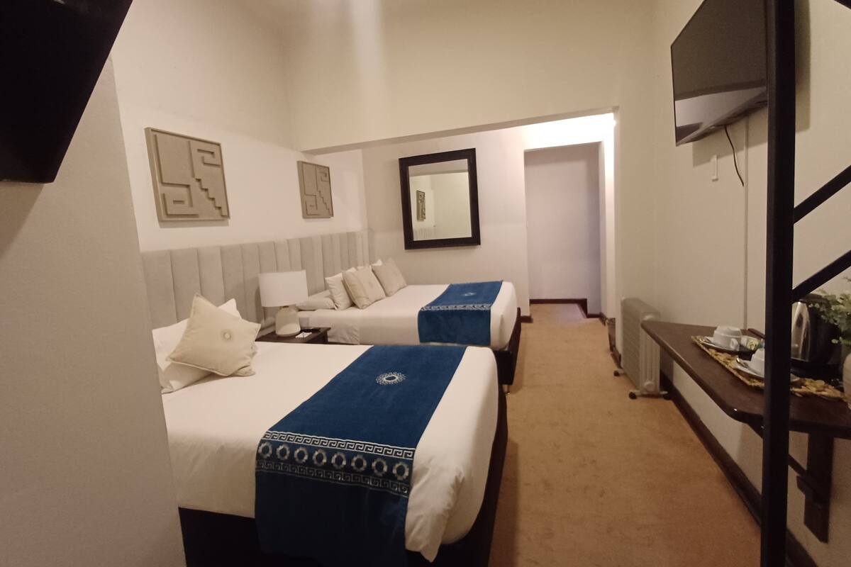 A hotel room with two beds, a TV, a desk, and a mirror.