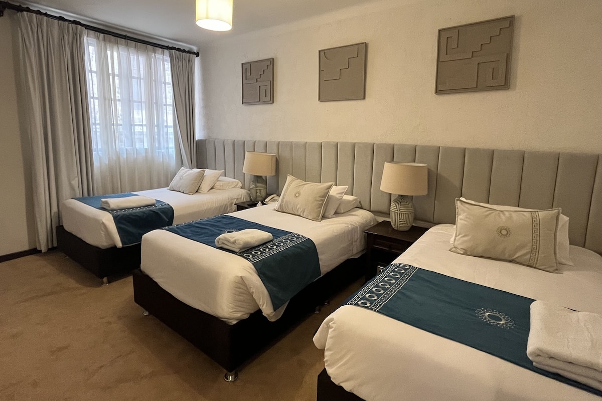 A hotel room with two beds, a large window with curtains, a hanging light fixture, and wall art.