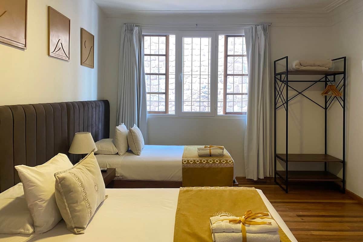 A hotel room with a bed, a sofa, a window with curtains, a wooden floor, and a metal shelf.