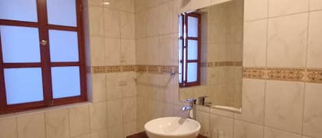 A bathroom with a white sink, a mirror, a toilet, and a window with a wooden frame.