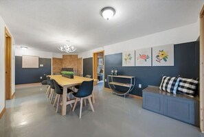Un espace repas moderne avec une table et des chaises en bois, un mur décoratif en briques et un canapé bleu agrémenté d’un coussin à carreaux.