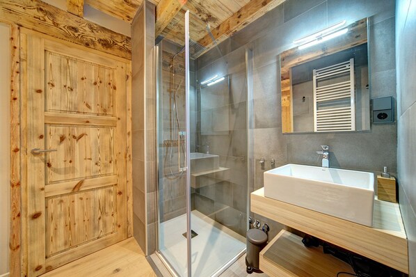 A modern bathroom with a wooden door, a glass shower enclosure, and a large sink with a mirror. - Espectacular Casa en Baqueira (Baqueira)