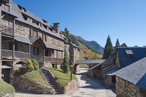 A stone building with a balcony, a staircase leading to a lower level, and a mountain in the background.