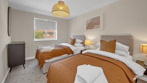 A hotel room with two beds, a wardrobe, a window with a view, and a hanging light fixture.