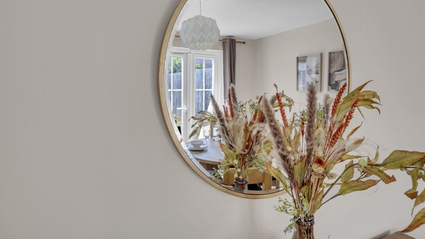 A round mirror on a wall with a reflection of a dining area, a window, and a hanging light fixture.