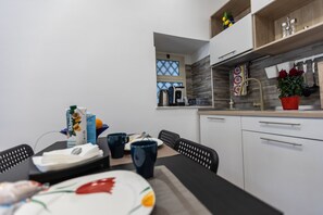 A modern kitchen with white cabinets, a window, and a dining area with a table set for two. - Al Castello-Independent house- Holiday home in Catania (Catania)