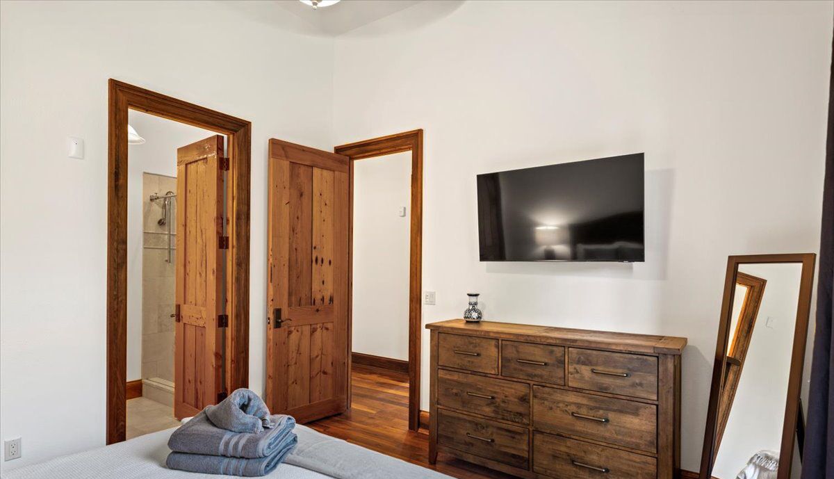 A bedroom with a wooden dresser, a flat-screen TV, and a bed with a folded towel.