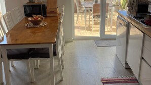 Una cocina moderna con comedor, que presenta una mesa de madera, sillas blancas y un gran ventanal corredizo que da a un patio exterior.