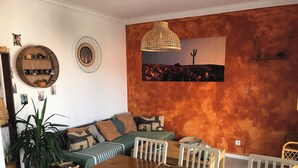 Comedor con mesa de madera y sillas blancas, rodeado por un sofá con cojines estampados.