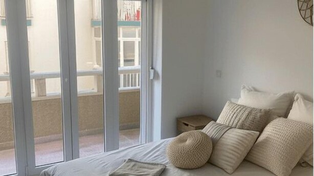 Un dormitorio con una cama grande, una lámpara colgante y vistas a un balcón exterior a través de puertas correderas de vidrio.