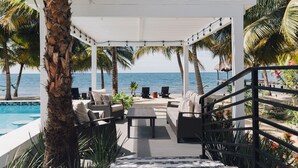 Un espacio de estar al aire libre cubierto con piscina, palmeras y vista al océano.
