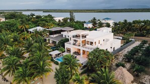 Un moderno resort de dos pisos con piscina, rodeado de palmeras y una playa.