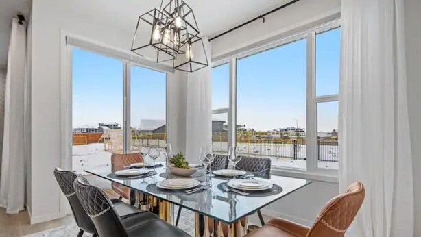 Un coin repas avec une table en verre, des chaises noires et marron, et une vue sur la ville grâce à de grandes fenêtres.