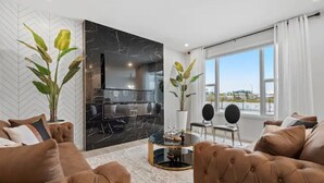 Un salon moderne avec un ensemble de canapés marron, un mur d’accent en marbre et une vue sur l’extérieur grâce à de grandes fenêtres.