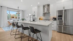 Une cuisine moderne dotée d’un îlot central, d’appareils électroménagers en acier inoxydable et de tabourets de bar.