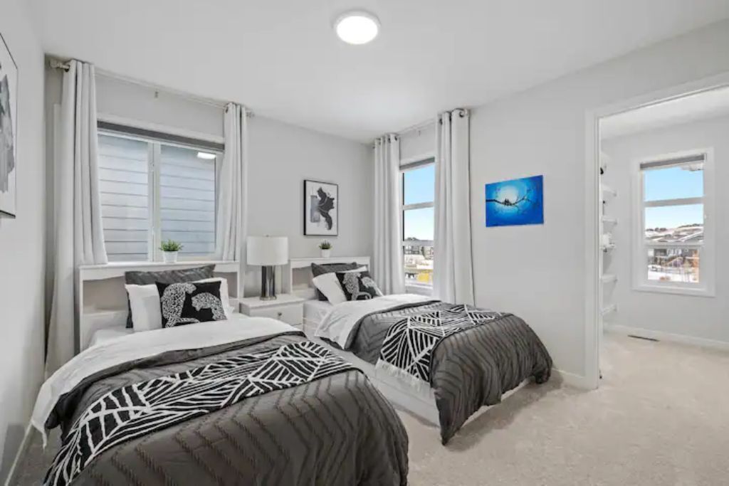 A bedroom with two beds, white walls, and a city view through the window.