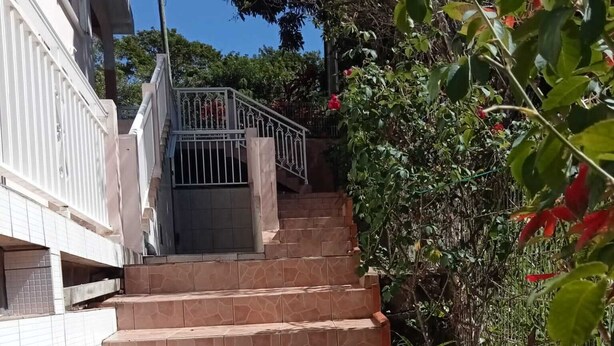 A set of stone steps leading up to a gated entrance, surrounded by lush greenery and flowering plants. - Maison en rez de Jardin, à 10 Minutes de la mer (Le Morne-Vert)