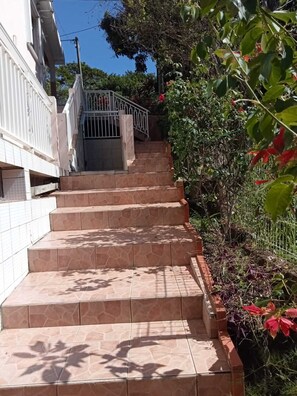 A set of stone steps leading up to a gated entrance, surrounded by lush greenery and flowering plants. - Maison en rez de Jardin, à 10 Minutes de la mer (Le Morne-Vert)