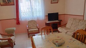 A dining area with a table set for four, surrounded by wooden chairs. There is a television on a stand to the right. - Maison en rez de Jardin, à 10 Minutes de la mer (Le Morne-Vert)