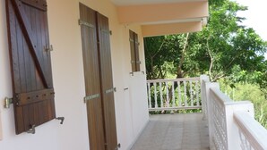 A covered balcony with a tiled floor, wooden doors, and a white railing. - Maison en rez de Jardin, à 10 Minutes de la mer (Le Morne-Vert)