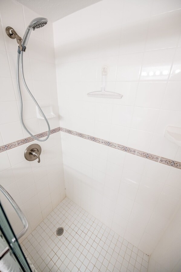 A shower area with a handheld showerhead, a wall-mounted faucet, and a shower control knob. - Oceanfront Charmer (Ormond Beach)