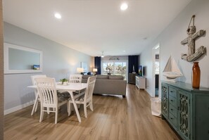 A modern living room with a dining area, a sofa, a TV, and a view of the beach. - Beachfront Bliss: 2/2 with Stunning Gulf Views! (Longboat Key)