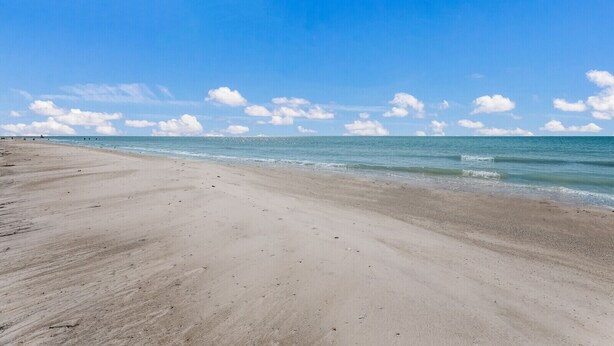Una playa extensa de arena clara con olas suaves y un cielo azul despejado.