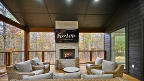 Un rincón al aire libre acogedor con muebles de mimbre, una chimenea de piedra y un cartel de TreeLine Vacation Rentals.
