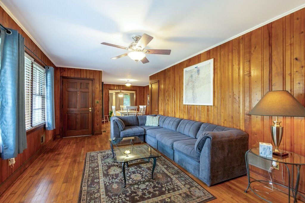 A living room with wooden paneling, a ceiling fan, a sectional sofa, a glass coffee table, and a lamp.