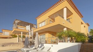 A two-story building with a balcony, a pool area with sun loungers, and palm trees. - My Island Escape (Santiago del Teide)