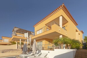 A two-story building with a balcony, a pool area with sun loungers, and palm trees. - My Island Escape (Santiago del Teide)