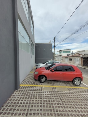 A parking area with a red car parked in front of a building with a grey facade. - Hotel Manaus - Dom Pedro (Manaus)