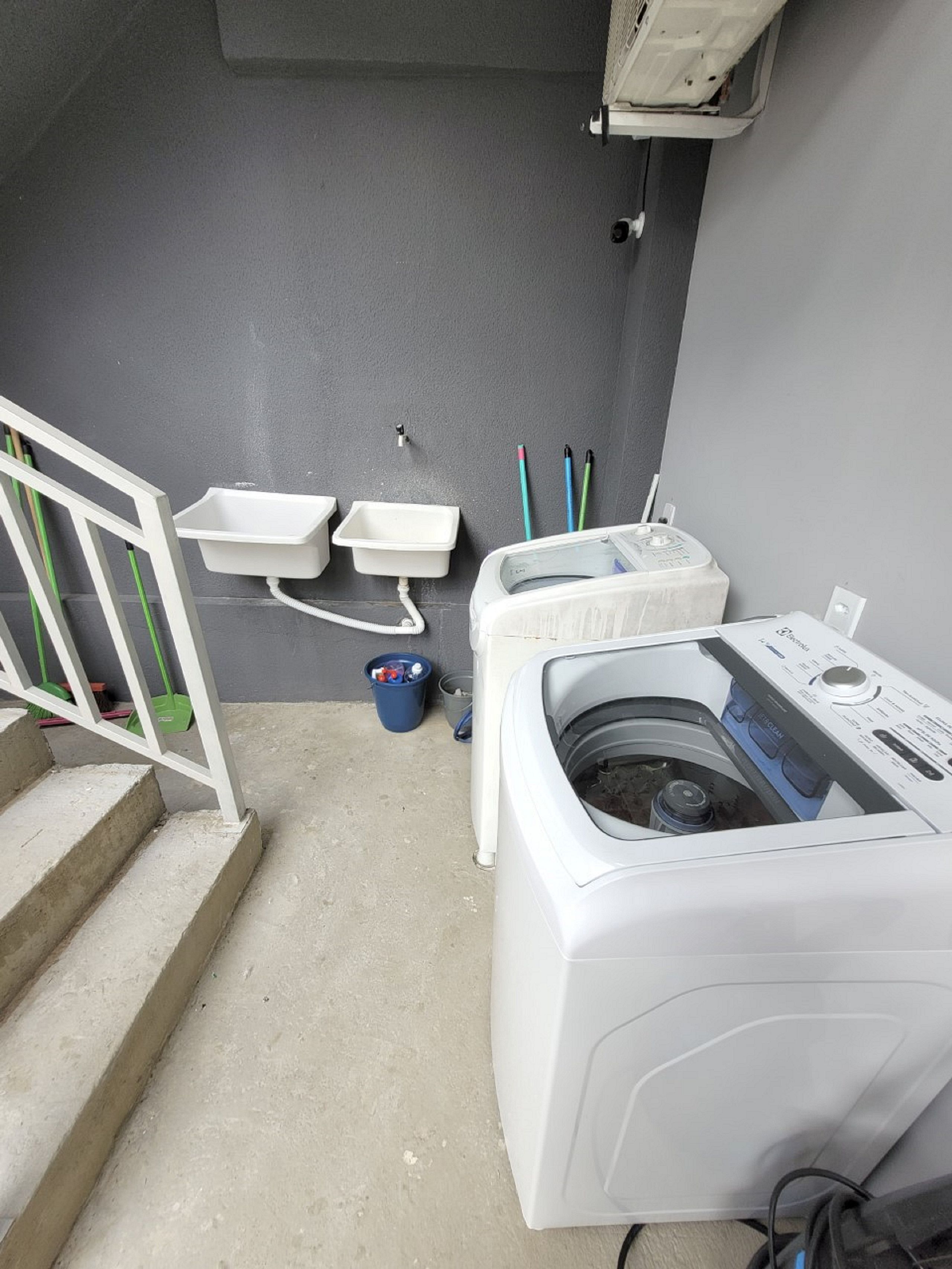 Una sala de bugaderia amb una rentadora, dues banyades i un cubet blau.