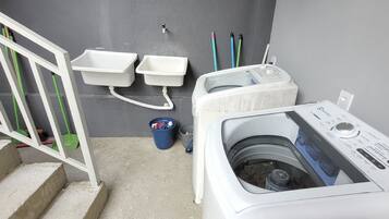 Una sala de bugaderia amb una rentadora, dues banyades i un cubet blau.