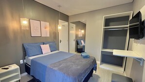 A modern bedroom with a bed, bedside tables, a wardrobe, a TV mounted on the wall, and a small seating area. - Hotel Manaus - Dom Pedro (Manaus)