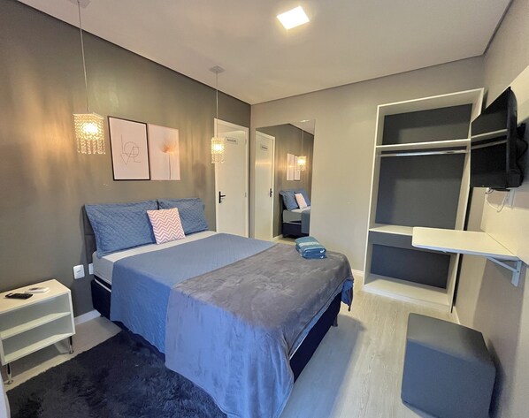 Une chambre moderne comprenant un lit, des tables de chevet, une armoire, un téléviseur fixé au mur et un petit coin salon.