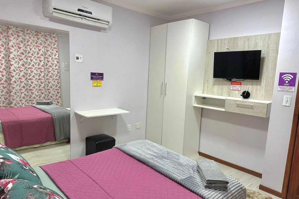A hotel room with two beds, a wardrobe, a TV, and a small desk.