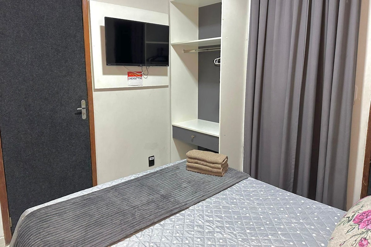 A hotel room with a bed, a TV mounted on the wall, a wardrobe, and a curtain.