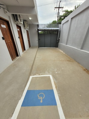 A narrow corridor with a blue handicapped parking space, a grey gate, and a white wall with a door labeled 'QUARTO 02'. - Hotel Manaus - Dom Pedro (Manaus)